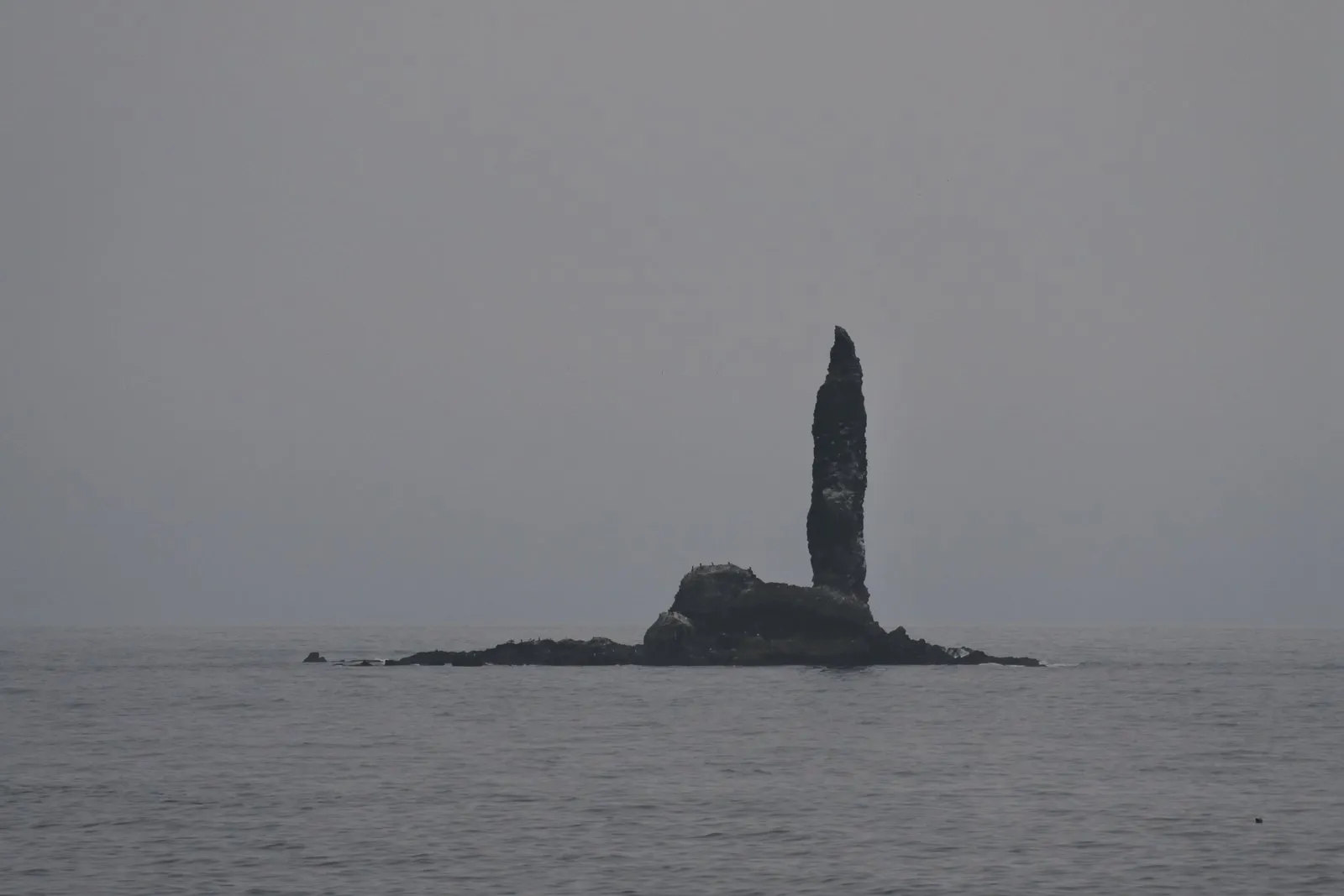 灰色の海に浮かぶ岩礁と、そこから細く立ち上がる岩の柱（ローソク岩）