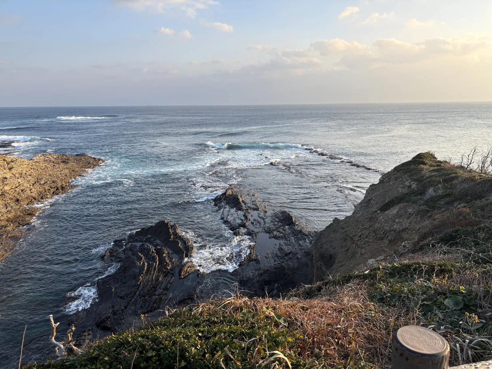 殿崎の朝。岬の先の岩礁に白波が砕け、朝日で海面が光っている